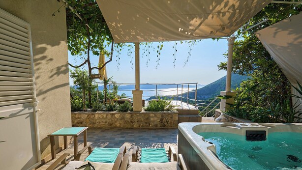 Un área de descanso al aire libre iluminada por el sol, con un jacuzzi, sillones y vistas al mar y las montañas.
