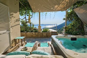A sunlit outdoor lounge area with a hot tub, lounge chairs, and a view of the sea and mountains. - House Lillla (Dubrovnik)