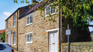A stone building with a white door and windows, a parked car, and a parking sign. - 2 bedroom accommodation in Richmond (Richmond)
