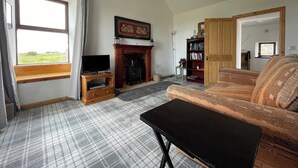 A living room with a fireplace, a television on a wooden stand, a sofa, and a patterned rug. - You will love everything about Mey Bee. (Mey, near Thurso)