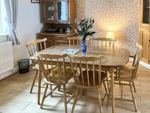 A wooden dining table with chairs, a vase with flowers, and a kitchen area with cabinets and a radiator.