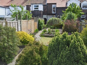 A residential garden with a pathway, various shrubs, and a wooden fence.
