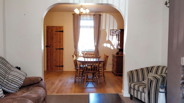 Ein Wohnzimmer mit braunem Sofa, einem gestreiften Sessel, einem dunklen Couchtisch und einem Essbereich mit Holztischen und -stühlen.