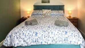 Ein Bett mit Blumenmuster, zwei Nachttische mit Lampen, ein Kopfteil und ein Wandbild.