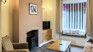 Ein Wohnzimmer mit Kamin, Fernseher, Sofa, Couchtisch und einem fenster mit Vorhängen.