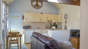 A cozy living room with a leather sofa, wooden dining table, and a kitchen area with light-colored cabinets and a wooden ceiling.
