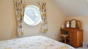 A bedroom with a bed, a dresser, a mirror, and a window with curtains.