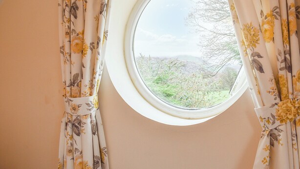 A window with floral curtains and a view of a green landscape.