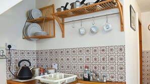 A kitchen with a wooden cabinet, a kettle, a sink, and a shelf with dishes and pots.