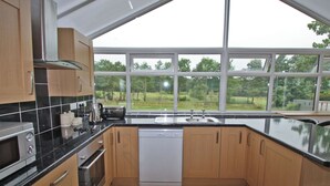 Una cocina moderna con armarios de madera, encimera negra y lavavajillas. Cuenta con ventanas amplias que ofrecen vistas a un paisaje verde.