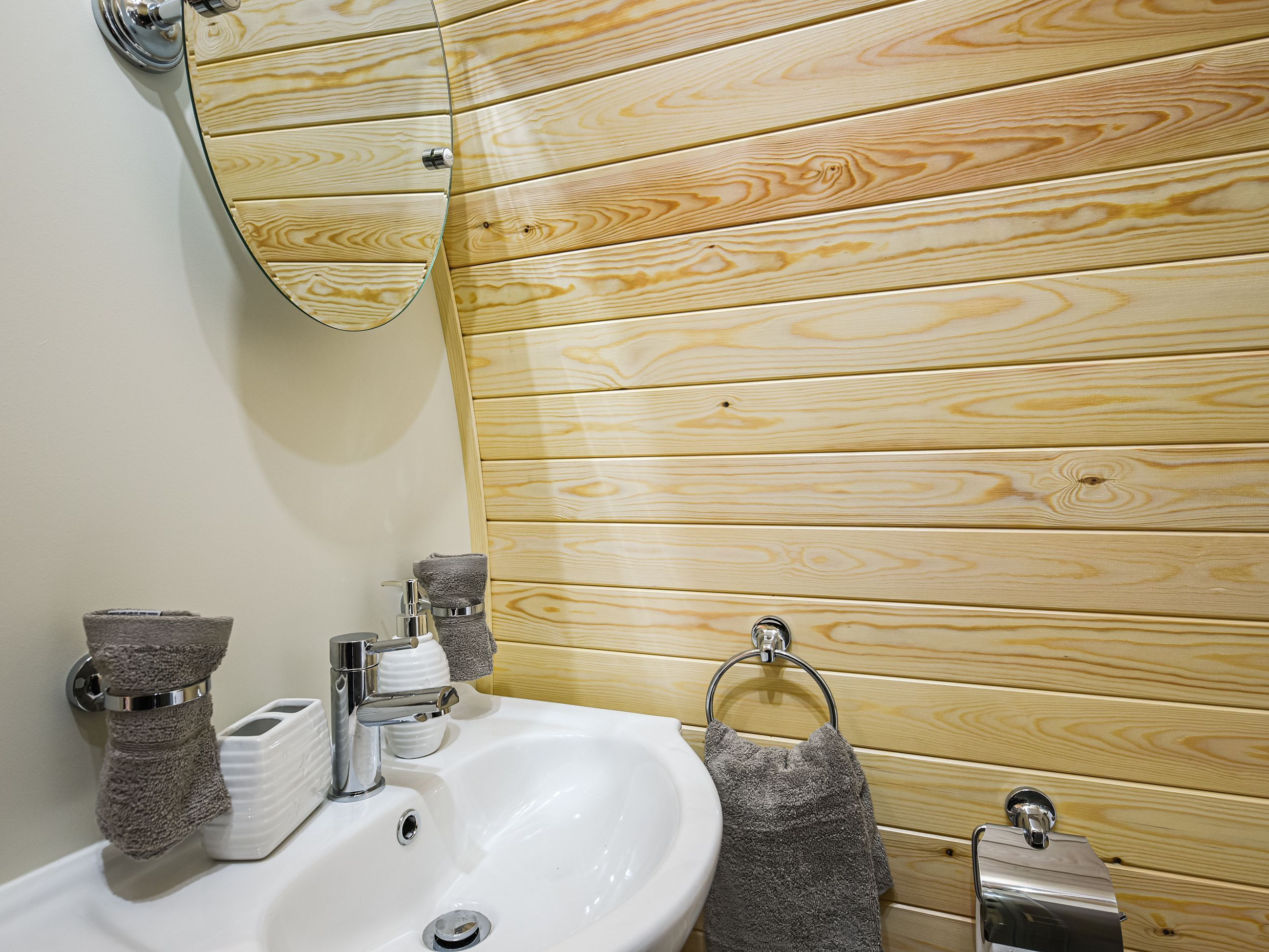 Un baño con pared de paneles de madera, un lavamanos blanco, un espejo y un perchero para toallas.