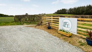 En grussti, der fører til en træport med et skilt, der viser 'Podiau Efrynwyp Pods Camping'.