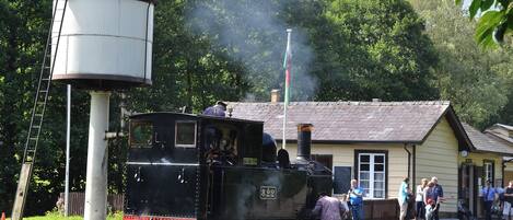 A steam locomotive at a station with a water tower, platform, and passengers.