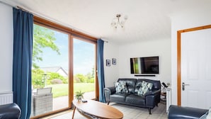A living room with a sofa, a coffee table, and a TV mounted on the wall. - 4 bedroom accommodation in Brodick (Brodick)