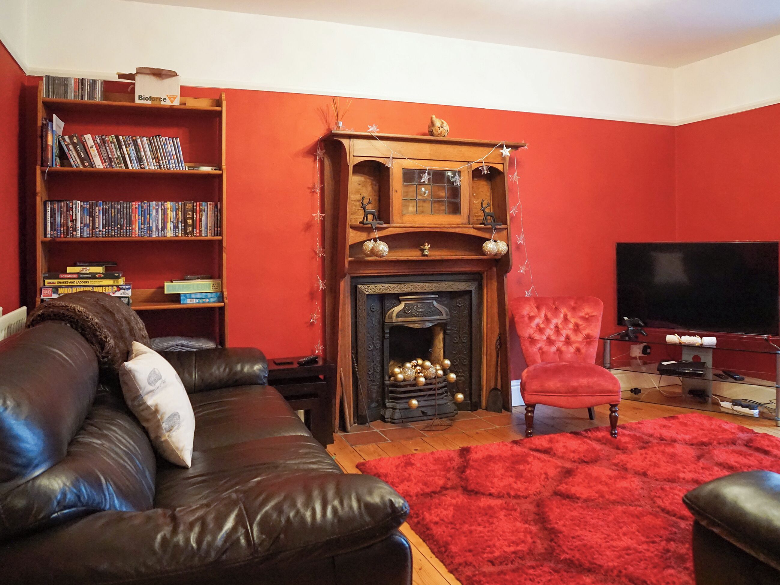 En stue med pejs, bogreol, lædersofa, rød måtte og fjernsyn.