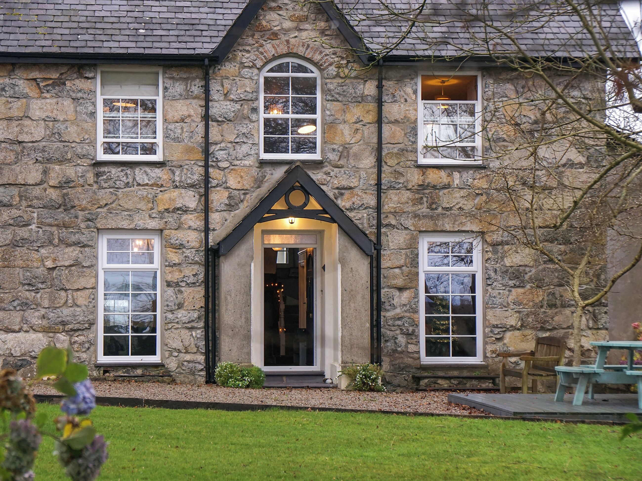 A stone building with a central entrance, multiple windows, and a small outdoor seating area.