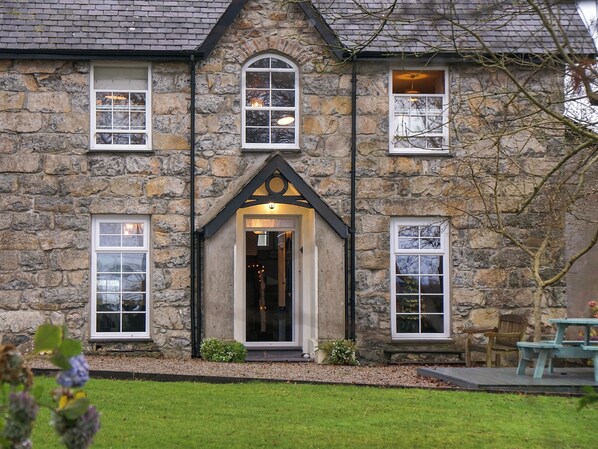 A stone building with a central entrance, multiple windows, and a small outdoor seating area.