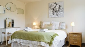 Un dormitorio con cama, lámparas de noche, cómoda, espejo y un cuadro en la pared.