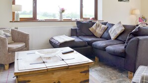 Una sala de estar con sofá, sillón y una mesa de centro con un tazón y controles remotos.