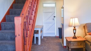 Un escalier avec des balustrades en bois, des marches recouvertes de moquette, une porte blanche, une petite table, une lampe et une chaise.