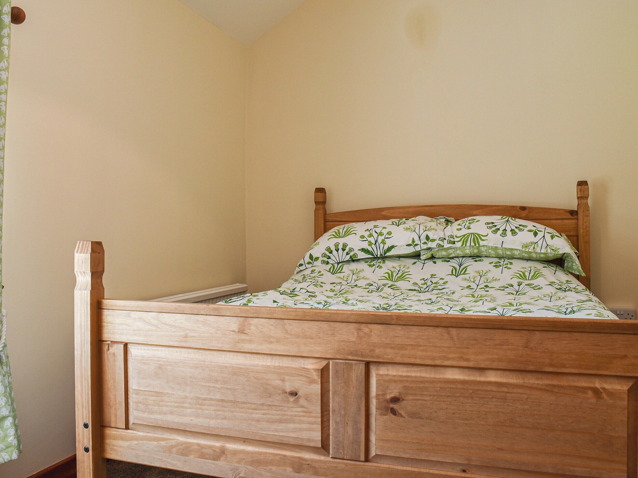 A wooden bed with a floral bedspread and pillows, a wooden headboard, and a simple room layout.