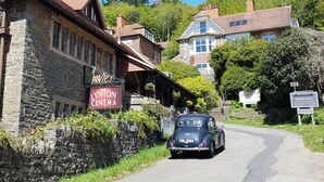 Une voiture ancienne est garée devant un cinéma à la façade en pierre, sur laquelle on peut lire l’inscription « Lynton Cinema ».