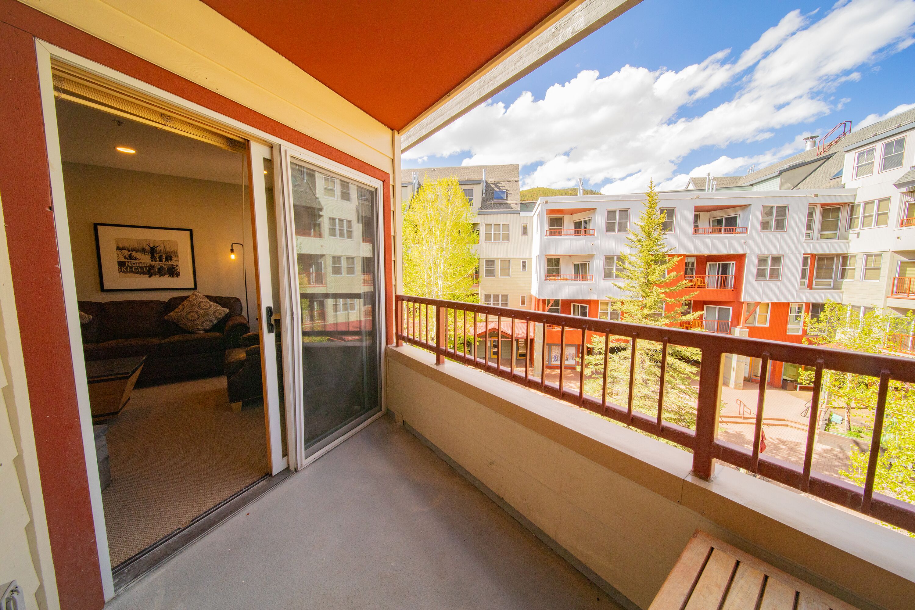 A balcony with a view of neighboring buildings and a door leading to a living area with a couch and a framed picture.
