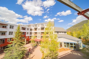 A multi-story building with balconies, a covered outdoor seating area, and a view of a mountain.