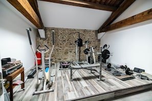 A gym with various exercise equipment, a stone wall, and wooden beams.