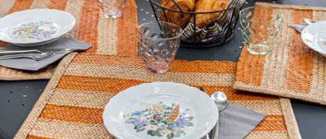 A table set outdoors with plates, glasses, and a basket of bread.