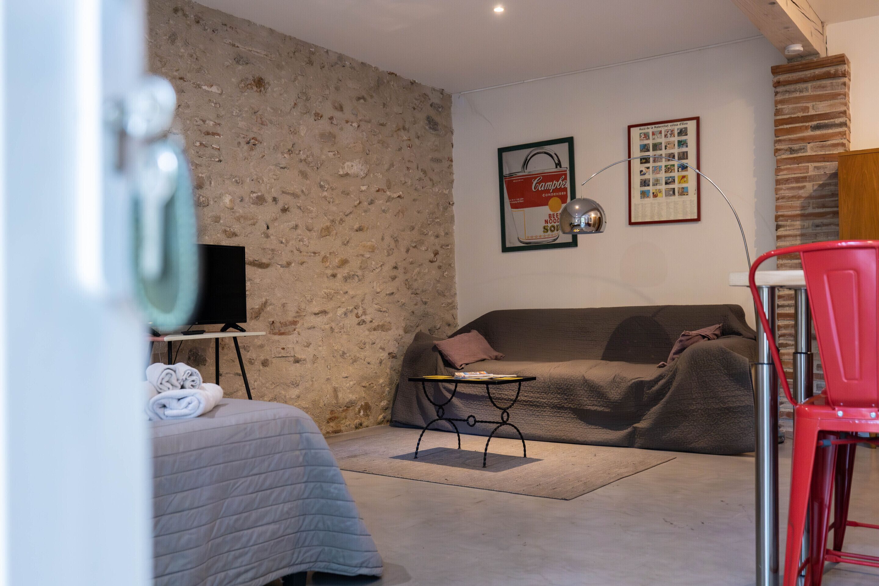 Une pièce chaleureuse avec un mur en pierre, une télévision, un fauteuil rouge et un canapé.