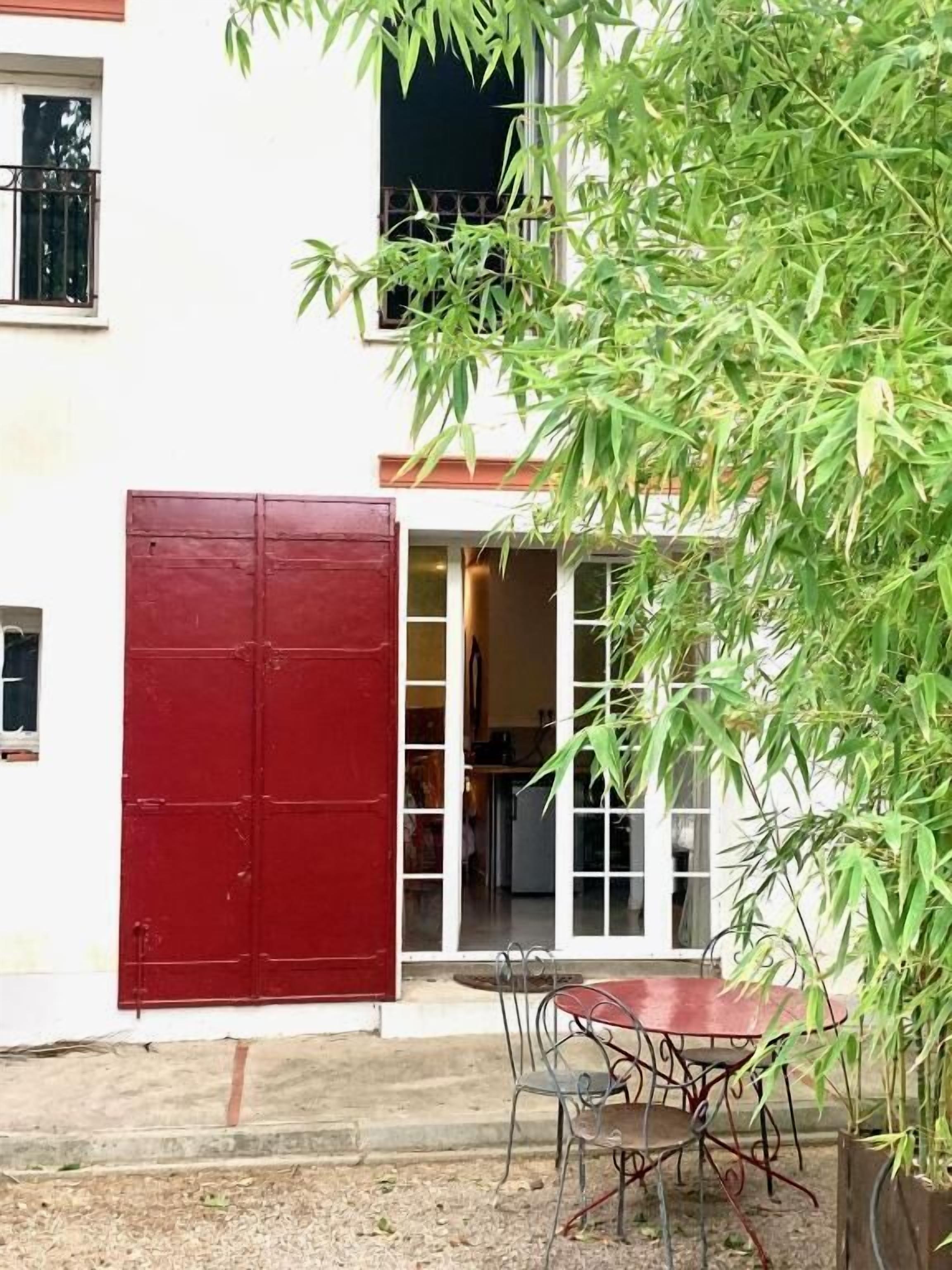 Un edifici amb una porta vermella, un vestíbul amb porta de vidre i una taula amb caires a l'exterior.