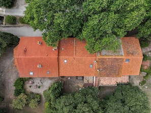 A large building with a red-tiled roof, surrounded by dense green trees.