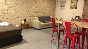 Ein Wohnzimmer mit Steinwand, einer Couch, einem Esstisch mit roten Stühlen und einem kleinen Beistelltisch mit Lampe.