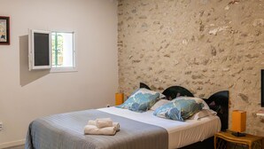 Ein Schlafzimmer mit einem Bett, einem Fenster, einer Steinwand und einem Nachttisch mit Lampe.