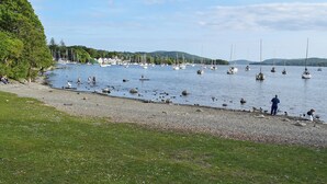 A lakeside view with boats, a grassy shore, and a forested background. - 1 bedroom accommodation in Bowness-On-Windermere (Bowness-On-Windermere)