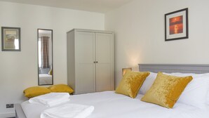 A neatly made bed with white linens and two mustard pillows, a white wardrobe, and a framed picture on the wall. - 1 bedroom accommodation in Bowness-On-Windermere (Bowness-On-Windermere)