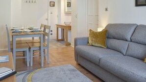 A modern living room with a grey sofa, a wooden dining table set with plates and glasses, and a small side table. - 1 bedroom accommodation in Bowness-On-Windermere (Bowness-On-Windermere)