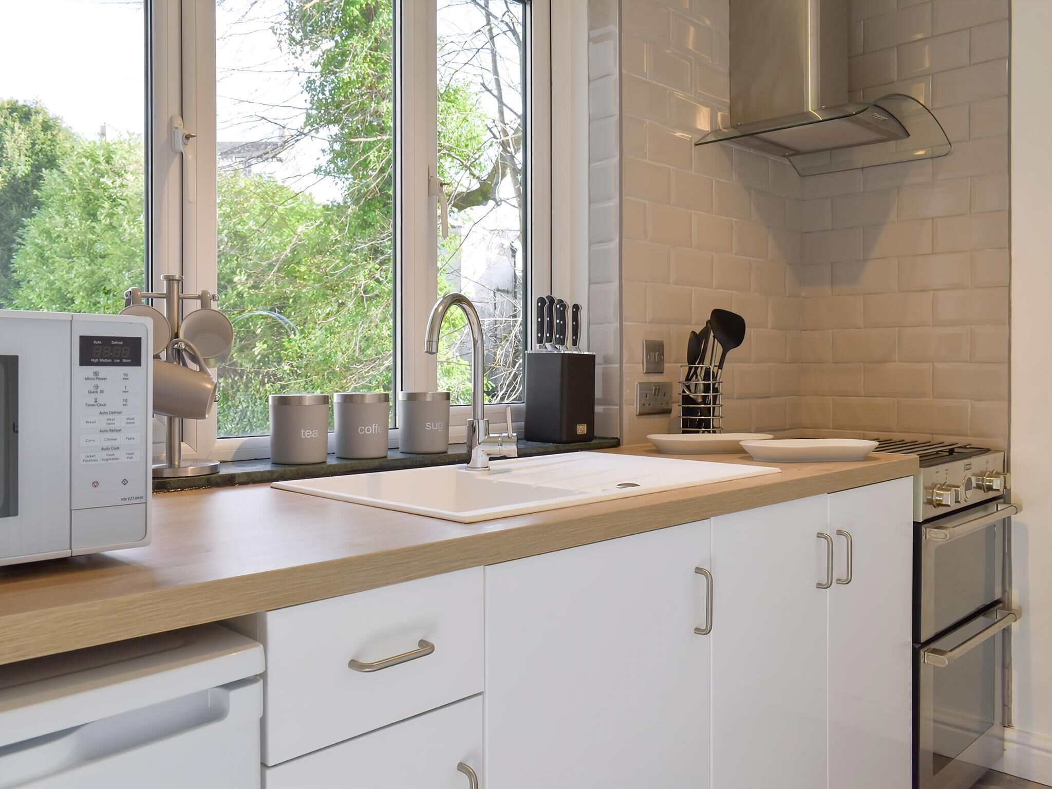 Une cuisine moderne dotée d’une grande fenêtre, de meubles blancs, d’un évier en acier inoxydable et d’une cuisinière encastrée.