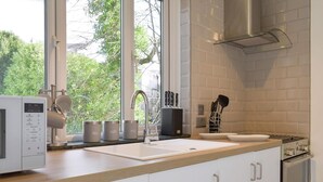 A modern kitchen with a large window, white cabinetry, a stainless steel sink, and a built-in stove. - 1 bedroom accommodation in Bowness-On-Windermere (Bowness-On-Windermere)