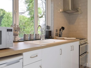 A modern kitchen with a large window, white cabinetry, a stainless steel sink, and a built-in stove.