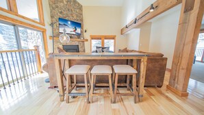 A kitchen with a wooden bar and stools, stone wall, and large windows. - Enclave 29 (Keystone)