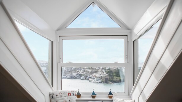 Habitació amb vista a una vila costanera a través d'una finestra gran i sostre inclinat.
