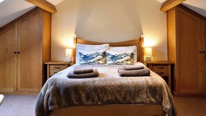 A bedroom with a sloped ceiling, wooden headboard, and a bed with a fluffy blanket and two pillows. - 2 bedroom accommodation in Dockray, near Ullswater (Dockray, near Ullswater)