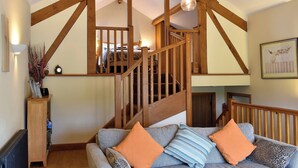 A spacious living area with a wooden staircase, a sofa with patterned cushions, and a radiator. - 2 bedroom accommodation in Dockray, near Ullswater (Dockray, near Ullswater)
