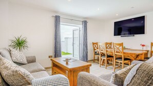 A living room with a sofa, a coffee table, a dining table with chairs, a TV mounted on the wall, and a plant. - Willow Tree Cottage - UK35893 (Ludchurch, near Narberth)