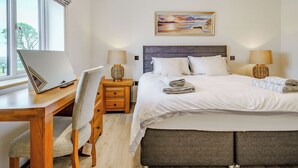 A bedroom with a bed, bedside lamps, a desk with a laptop, a chair, and a painting on the wall. - Willow Tree Cottage - UK35893 (Ludchurch, near Narberth)