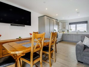 Une cuisine moderne avec des meubles gris, un coin repas avec une table et des chaises en bois, et un téléviseur à écran plat fixé au mur.