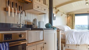 Uma cozinha compacta com fogão, forno e pia, e um quarto com cama e janela.