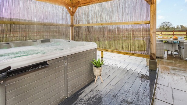 Un jacuzzi bajo una pérgola de madera con un fondo de valla de bambú.